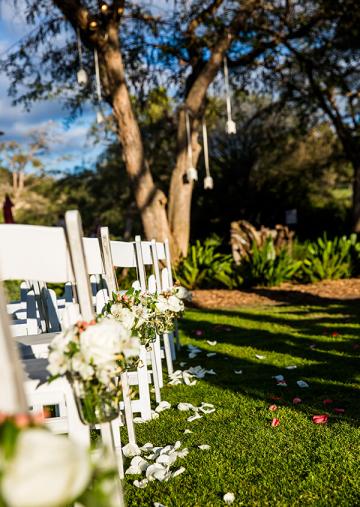 Closeup of wedding guest chairs with rose petals strewn on grass